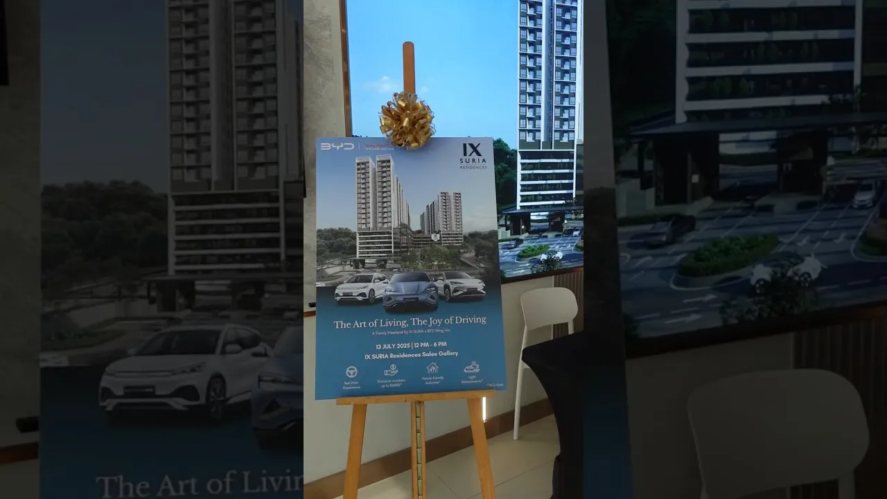 An IX SURIA x BYD “The Art of Living, The Joy of Driving” event poster on an easel in the sales gallery, showing the towers and three BYD cars
