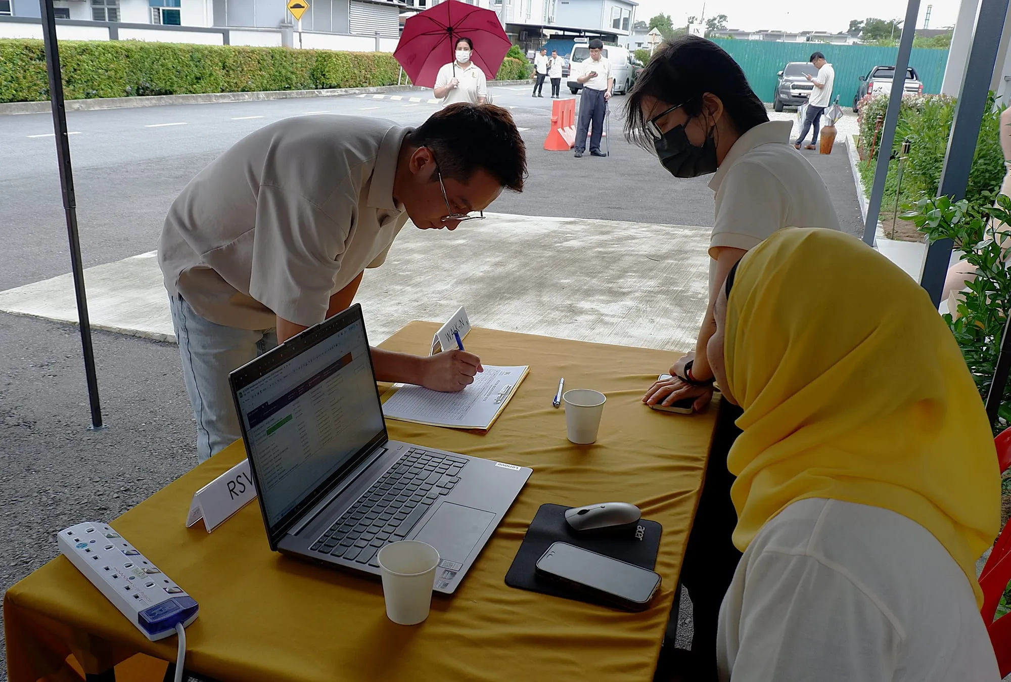 A guest signing in at the walk-in desk outside, two of the team helping at the laptop.