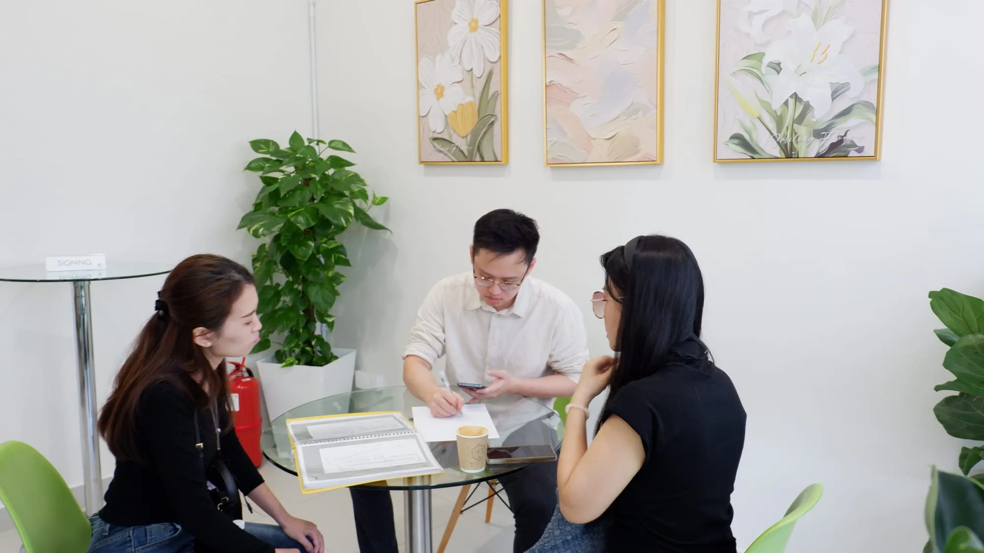 Three people going through paperwork at the signing table, framed flower prints on the wall.