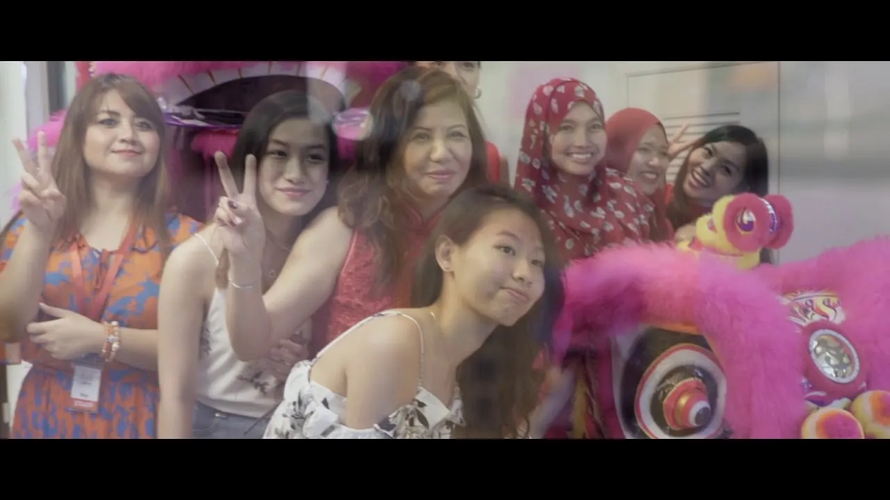 A group of women smiling and flashing peace signs beside a bright pink lion-dance costume at OnePark’s Chinese New Year open house
